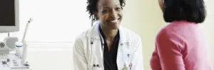 Female doctor talking to female patient in exam room, smiling